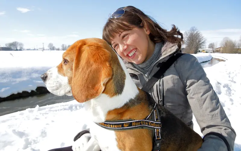 Owner looking at her dog as they both take in a snowy landscape