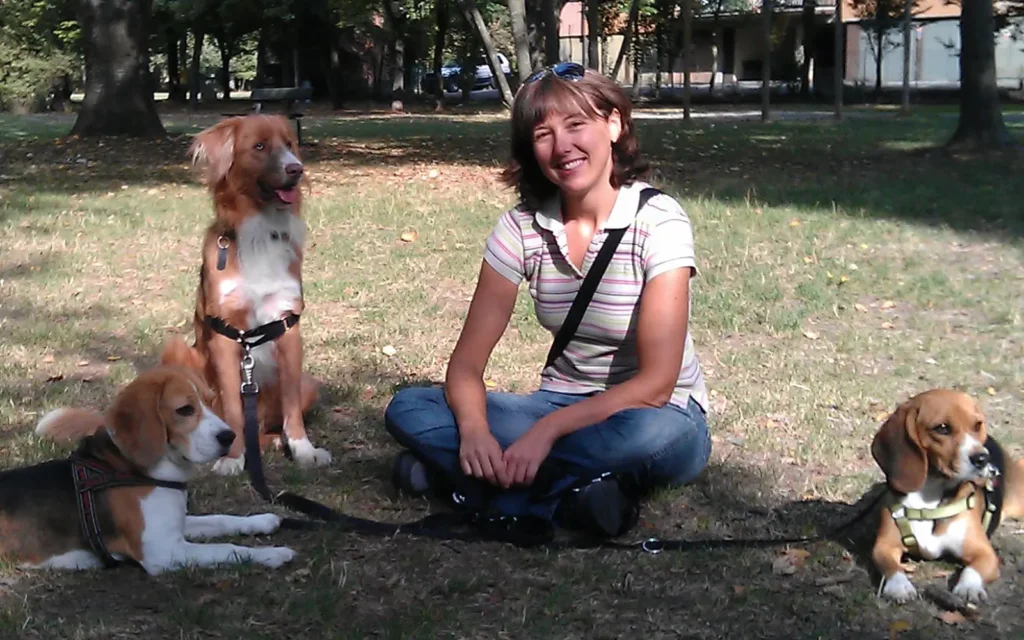 Dog trainer Simona sitting on the grass smiling with Diana the Beagle and two client dogs