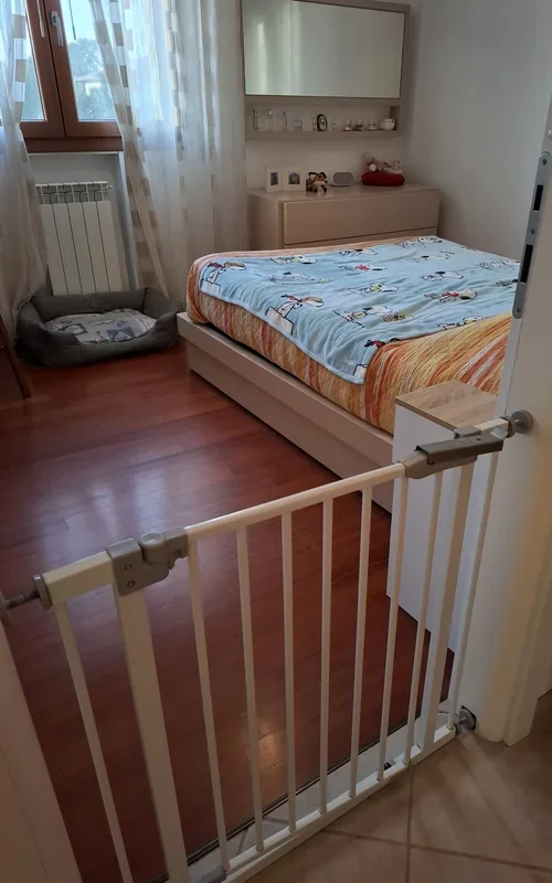Baby gate across a bedroom doorway, with an extra dog bed placed in the corner by the window